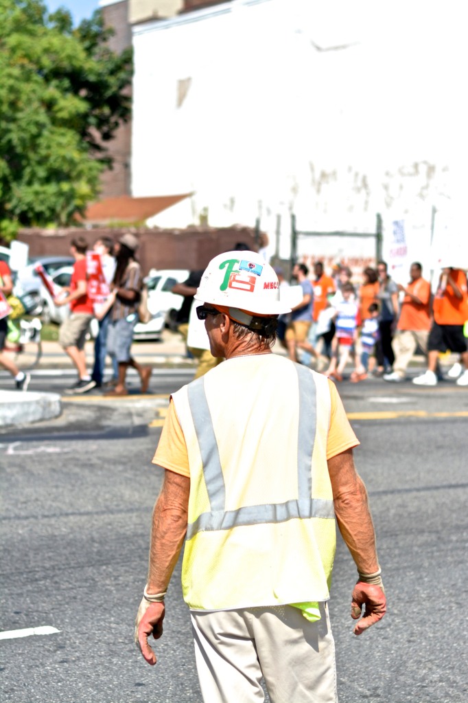 A construction worker pauses to watch march. 